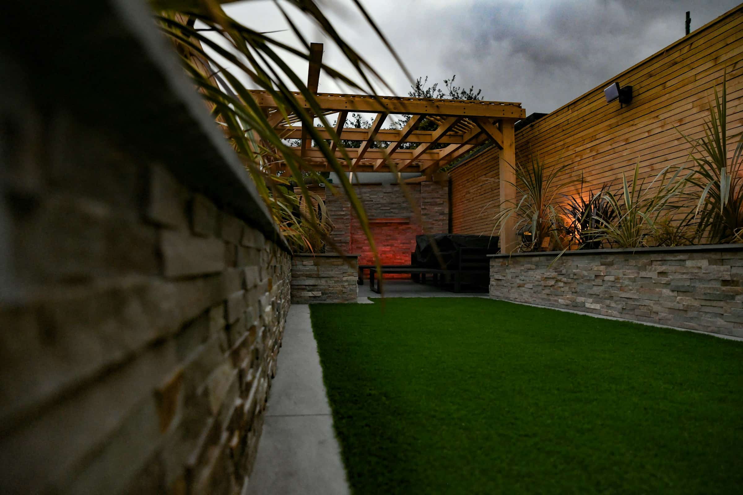 Backyard with new turf, a stone veneer wall, and a pergola at dusk